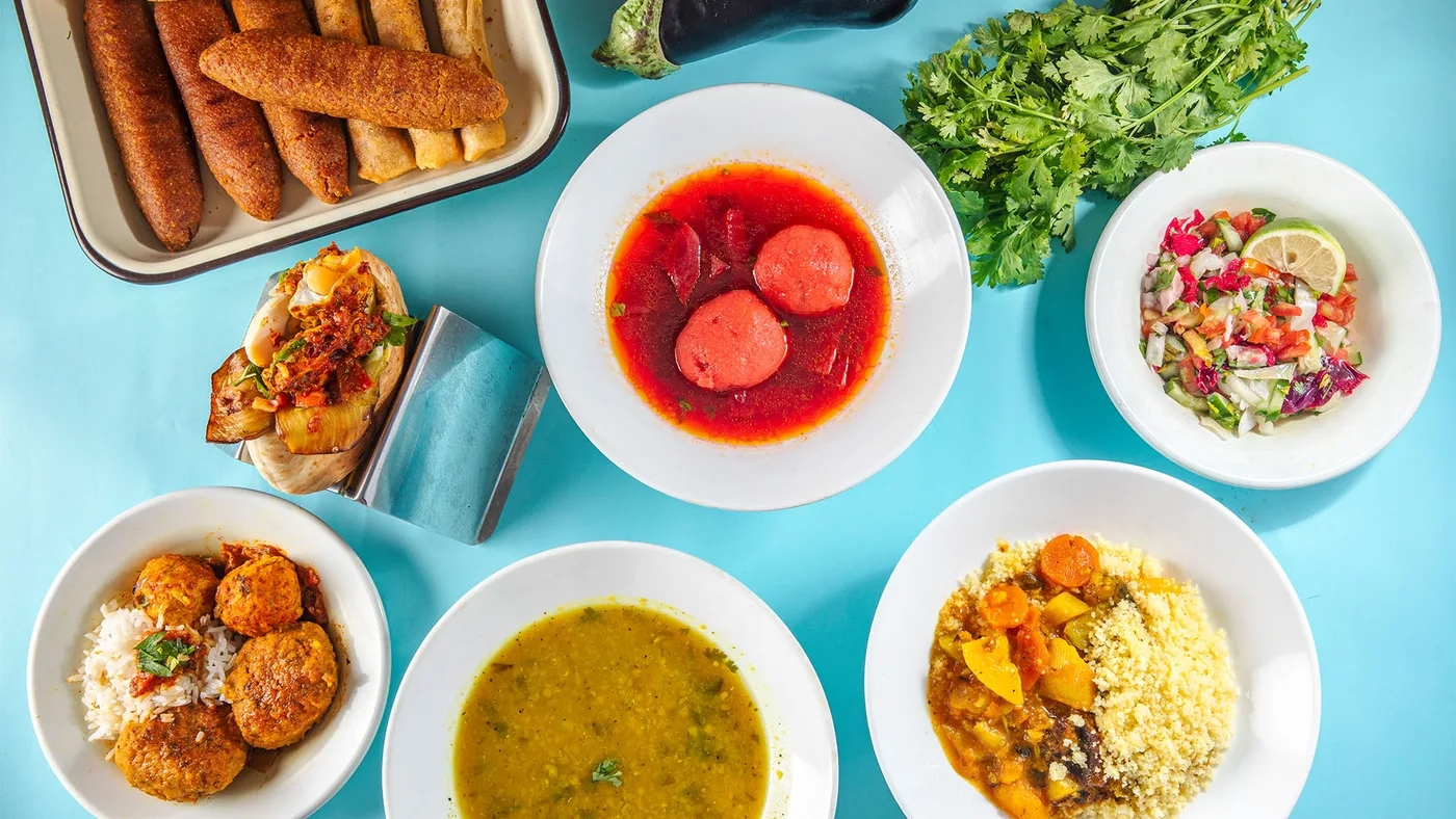Overhead spread of beet kubeh, couscous, meatballs, salad and additional dishes